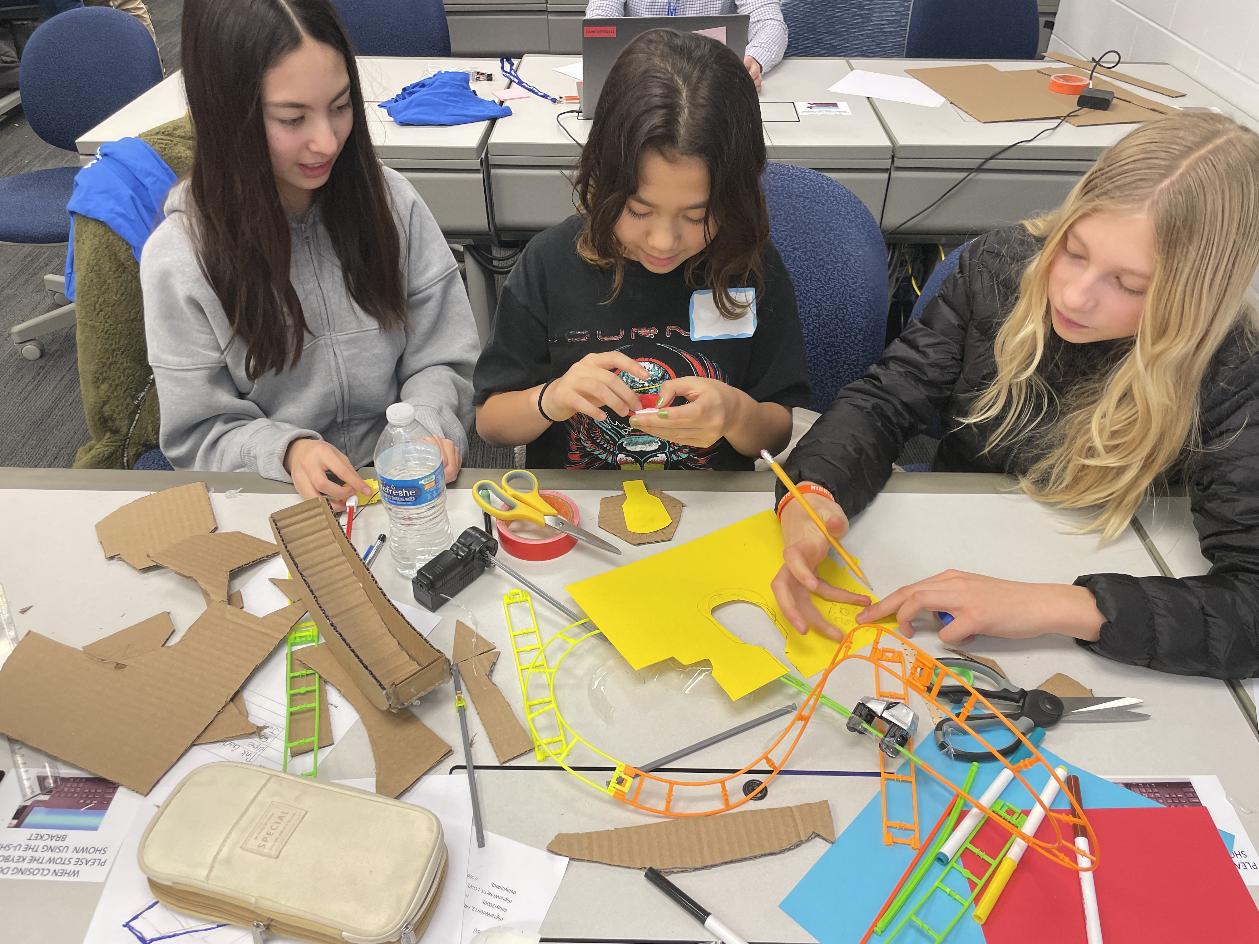 Three middle school students working together on a project using cardboard, construction paper, stencils and scissors.